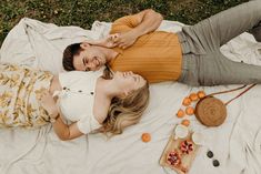 a man and woman laying on top of a blanket next to each other near oranges