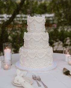 a white wedding cake sitting on top of a table next to silverware and candles