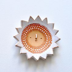 a white and orange clock with a face on it's face is mounted to the wall