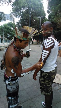 two men standing next to each other on a sidewalk with one holding something in his hand