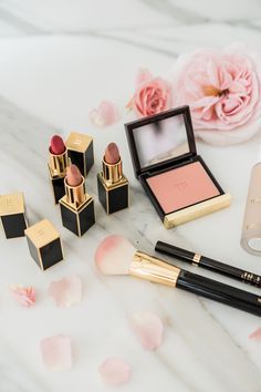 various makeup products on a marble surface with pink flowers and petals in the foreground