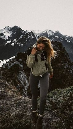 a woman walking on top of a mountain while listening to headphones with mountains in the background