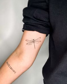 a woman's arm with a small dragonfly tattoo on it