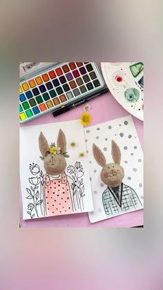 two paper rabbits are sitting next to each other in front of paintbrushes and watercolors