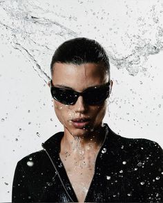 a woman wearing sunglasses and splashing water all over her face in front of a white background