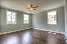 an empty room with hard wood flooring and two windows in the corner, all painted gray