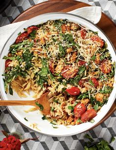 a white bowl filled with pasta and vegetables on top of a wooden serving platter