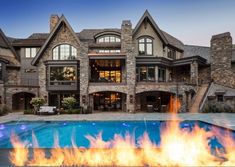 a fire pit in front of a large house with a swimming pool surrounded by stone walls