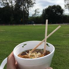 a person holding up a bowl of ramen with chopsticks in their hand