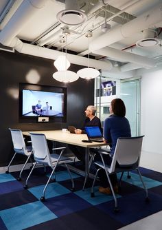 two people sitting at a table with laptops in front of a large screen on the wall