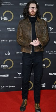 a man standing on top of a red carpet wearing a brown jacket and black pants