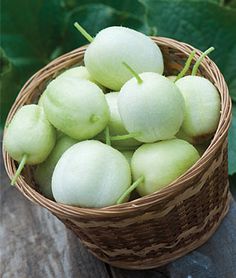 a wicker basket filled with green fruit on top of a wooden table next to leaves