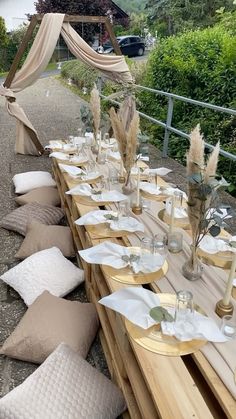 a long table set up with place settings for an outdoor dinner or party, along with flowers and candles