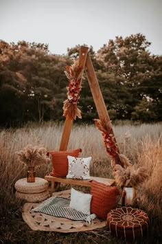 an outdoor seating area with pillows and blankets on the ground, surrounded by tall grass