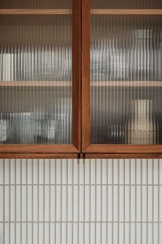 two wooden cabinets with glass doors in a white tiled kitchen countertop area, one is empty and the other is closed