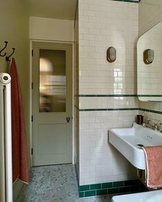 a bathroom with green and white tiles on the walls, two sinks and a mirror