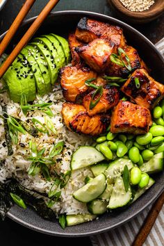 a bowl filled with rice, meat and vegetables next to chopsticks on the side