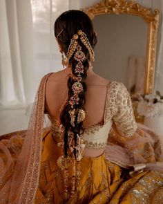 a woman with long hair wearing a yellow and gold dress sitting in front of a mirror