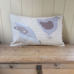 a pillow with two birds on it sitting on a wooden bench