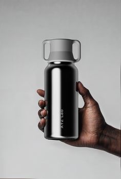 a hand holding a black and silver water bottle with the lid up in front of a gray background