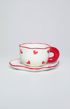 a cup and saucer with hearts painted on the side, sitting next to each other