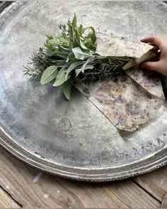 a person is holding some herbs on top of a metal platter that has been placed on a wooden table