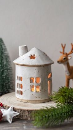 a small white house sitting on top of a wooden table next to christmas trees and ornaments