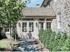 a stone house with white trim and windows on the front door is surrounded by greenery