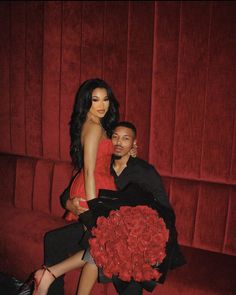 a man sitting next to a woman on top of a red couch in front of a red wall