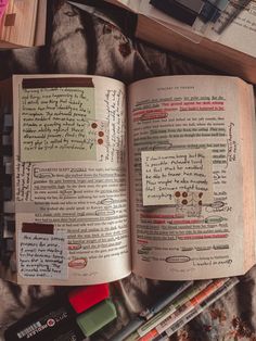 an open book sitting on top of a bed next to some pens and pencils