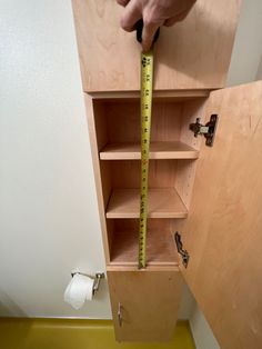 a person is measuring the height of a wooden cabinet with a tape measure on it