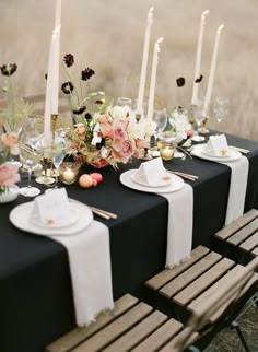 the table is set with white and black plates, silverware, flowers and candles