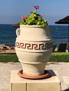 a large vase with flowers in it sitting on top of a cement block near the ocean