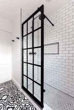 a black and white tiled bathroom with a glass shower door in the corner, next to a patterned floor