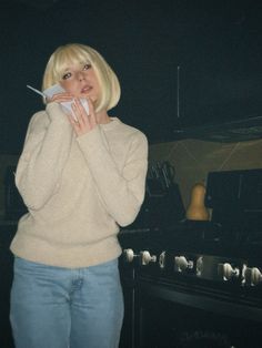 a blonde woman standing in front of an oven holding a napkin to her mouth and looking at the camera