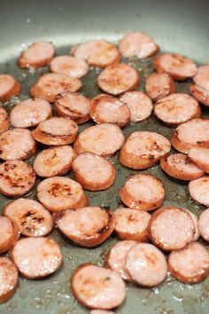 some sausages are cooking in a frying pan