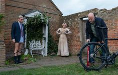 a man standing next to a bike in front of a brick building with two women