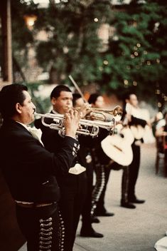 a band playing music on the sidewalk in front of some people wearing black and white outfits