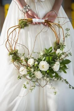 a woman in a white dress is holding a flower crown with greenery on it