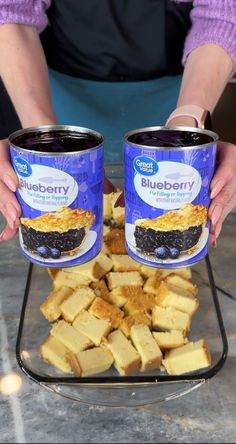 two people holding up cans of blueberry cheesecake on top of a pile of tofu