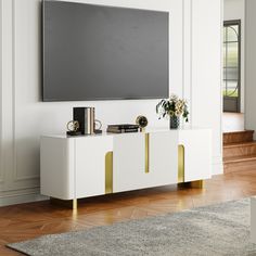 a white entertainment center with gold accents and a flat screen tv mounted on the wall