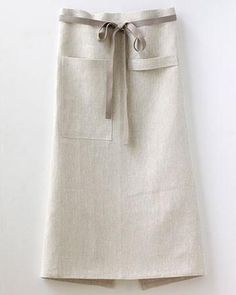 a white skirt with a tie on the waist and side pockets, hanging up against a wall