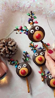 a hand is holding a stick with reindeer decorations on it and pine cones in the background