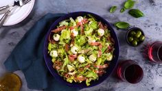 a blue bowl filled with salad next to glasses of wine and olives on a table