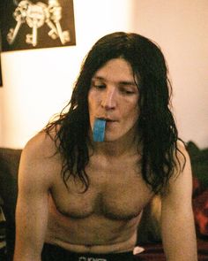 a man with long hair and no shirt is using an object in his mouth