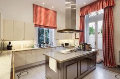 a large kitchen with an island in front of the stove and windows that have red checkered curtains on them