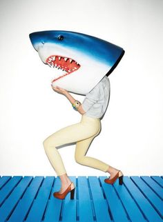 a woman holding a large shark pillow on top of her head while walking across a blue floor