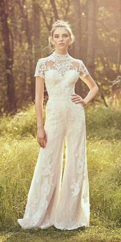 a woman standing in the grass wearing a white dress with sheer sleeves and lace detailing