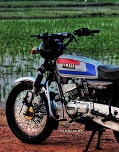 a motorcycle parked on the side of a dirt road in front of a rice field