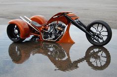 an orange motorcycle parked on top of a wet ground next to a parking lot filled with lots of water